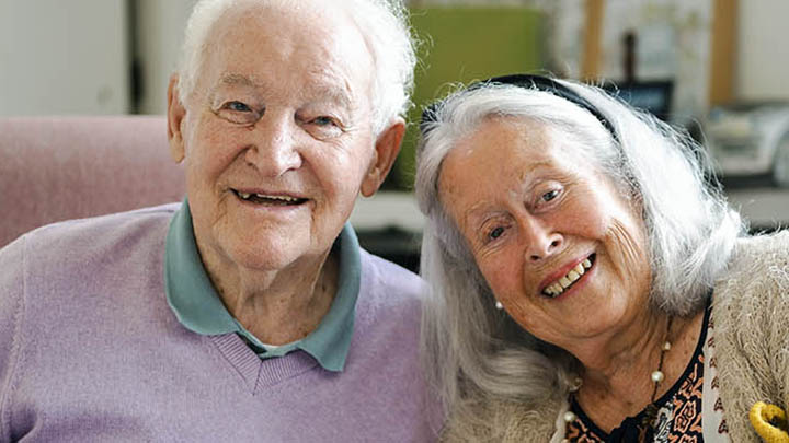 An elderly couple happily sitting side by side, smiling at the camera.