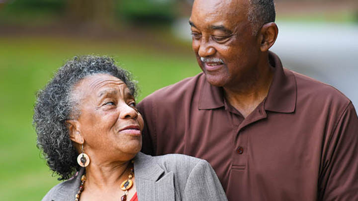 A mature couple smiling while standing outdoors in a park.