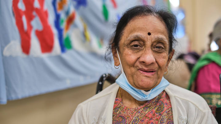 An older Asian woman with a mask below her chin.